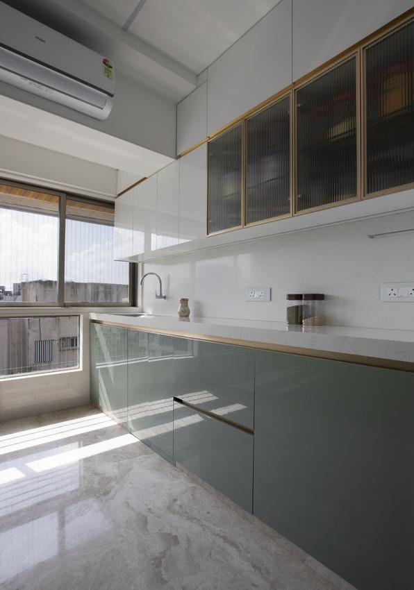 Sage green kitchen cabinets with brass-trimmed fluted glass upper units, sunlit